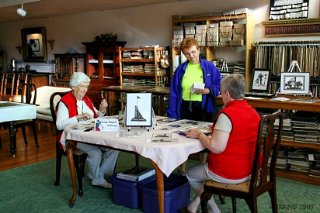 Elda Schiesser and daughter, Linda, demonstrating the art of Swiss Scherenschnitte to Carol Strause.